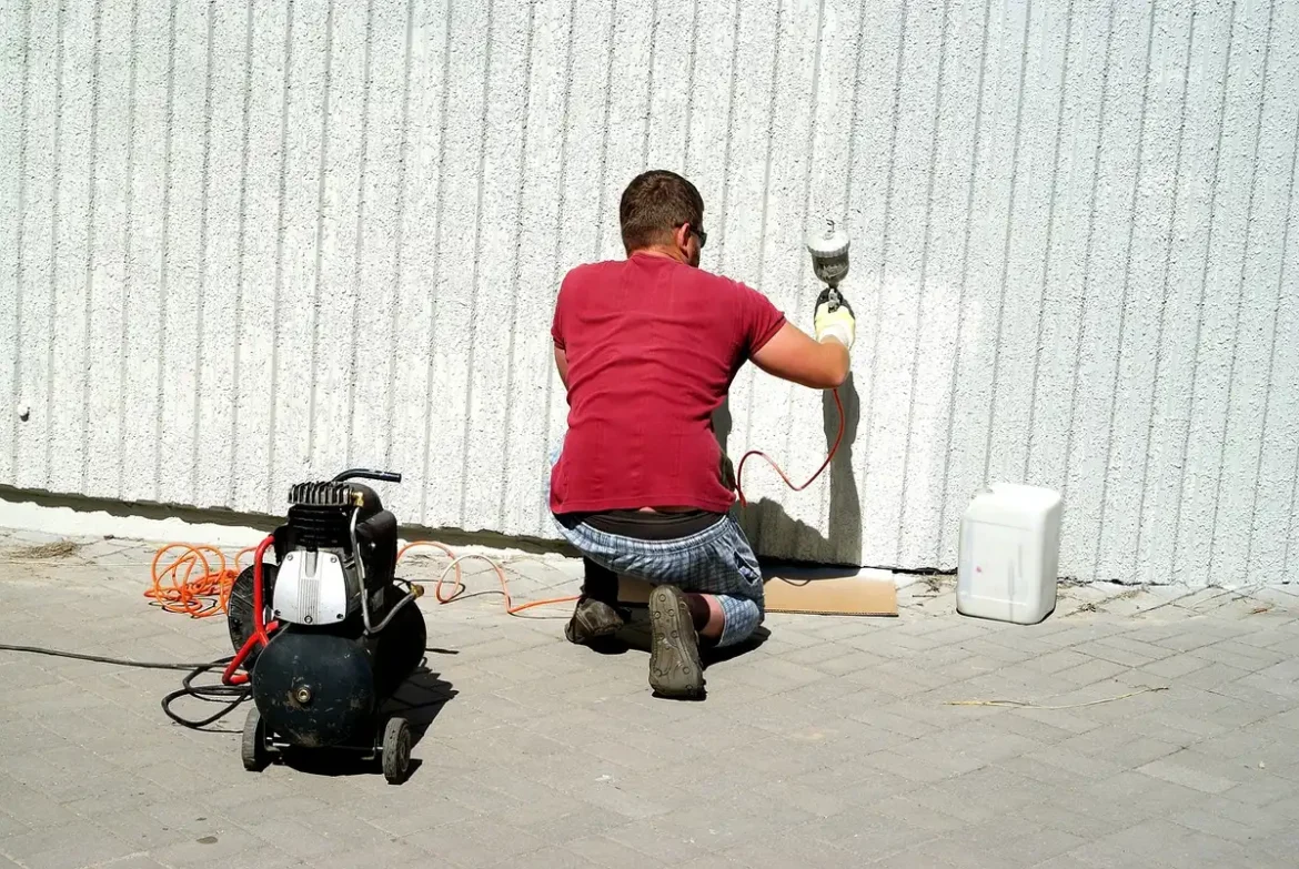 Atelier en journée: main tenant une bombe de peinture au-dessus d'une pièce métallique sur un établi